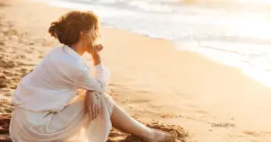 Kvinne sitter på stranden og ser utover